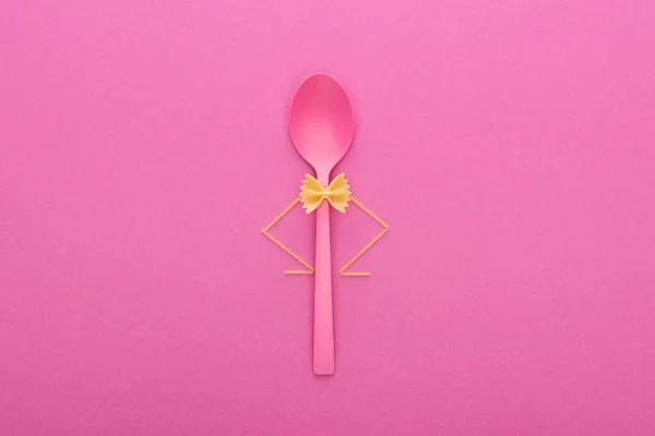 Pasta farfalle sin cocer en cuchara de plástico y espaguetis aislados en rosa - foto de stock