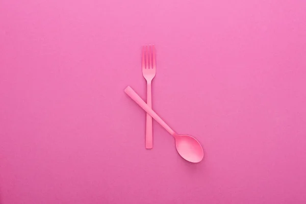 Crossed pink plastic fork and spoon isolated on pink — Stock Photo
