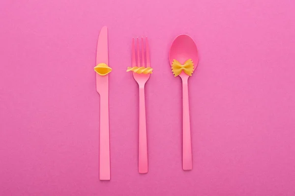 Vista dall'alto di diversi tipi di pasta su posate di plastica rosa isolate su rosa — Foto stock