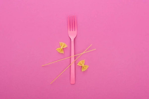 Rohe Farfalle-Pasta in der Nähe rosa Plastikgabel und Spaghetti isoliert auf rosa — Stockfoto