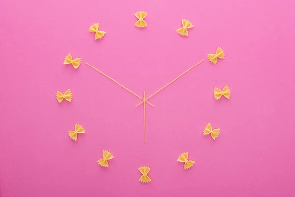 Вид сверху на концепцию часов с сырой фарфалле макароны и спагетти изолированы на розовый — стоковое фото