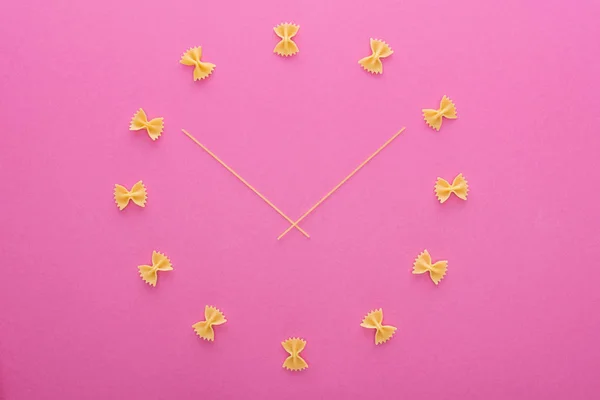 Vista superior do conceito de relógio com macarrão farfalle não cozido e espaguete no meio isolado em rosa — Fotografia de Stock