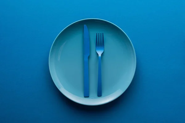 Blue plastic knife and fork on plate on blue background — Stock Photo