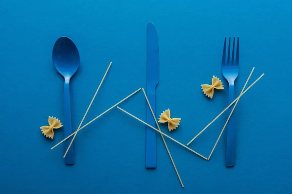 Cubiertos de plástico azul con espaguetis y pasta farfalle sobre fondo azul - foto de stock