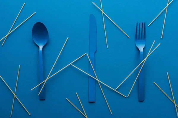 Couverts en plastique bleu avec spaghettis non cuits autour sur fond bleu — Photo de stock