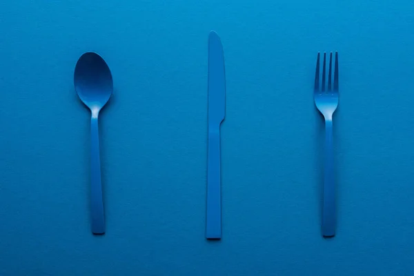 Cuillère, couteau et fourchette en plastique bleu sur fond bleu — Photo de stock