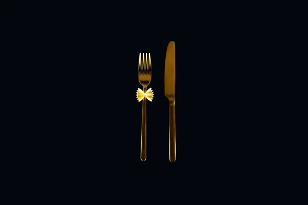 Uncooked farfalle pasta on metal fork near knife isolated on black — Stock Photo
