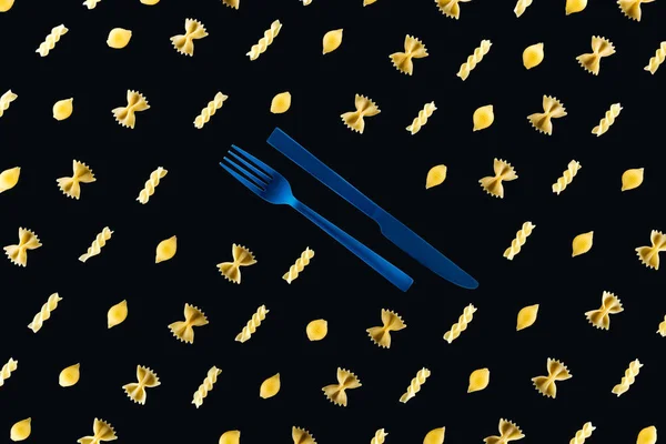 Disposición plana de diferentes tipos de pasta con tenedor azul plástico y cuchillo en medio aislado en negro - foto de stock