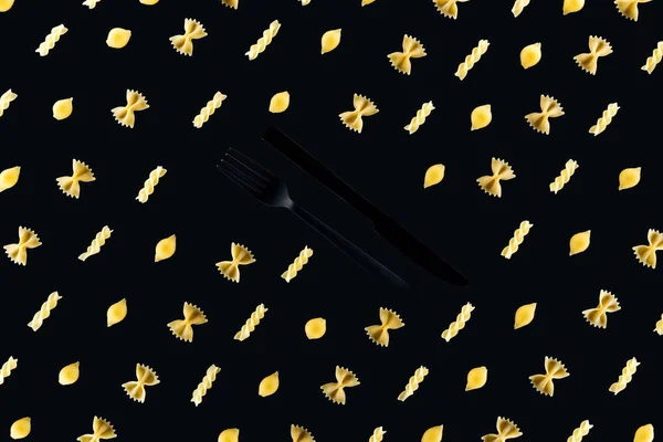 Disposición plana de diferentes tipos de pasta con tenedor de plástico negro y cuchillo en medio aislado en negro - foto de stock