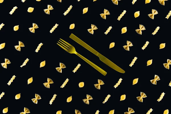 Плоский шар різних видів макаронних виробів з пластиковою жовтою вилкою і ножем посередині ізольовані на чорному — стокове фото