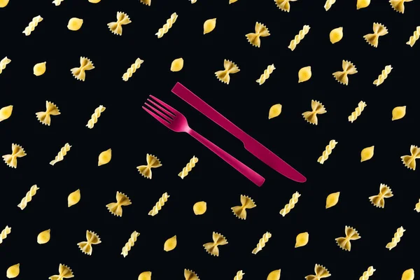 Flache Lage verschiedener Nudelsorten mit rosafarbener Gabel und Messer in der Mitte isoliert auf schwarz — Stockfoto