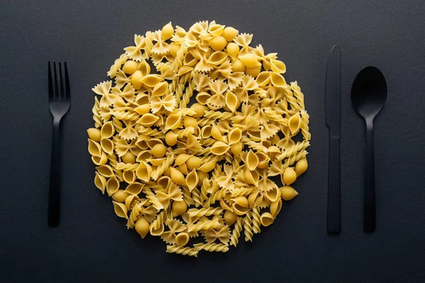 Vista dall'alto del concetto di piastra con forchetta in plastica nera, cucchiaio e coltello isolato su nero — Foto stock