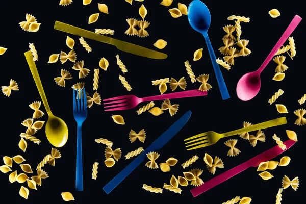 Top view of mixed colorful knives, forks and spoons with different kinds of pasta isolated on black — Stock Photo