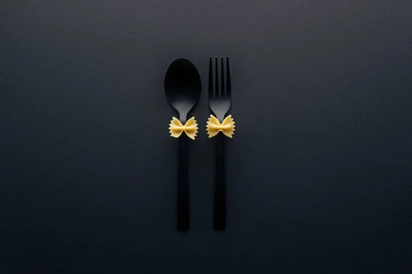 Uncooked farfalle pasta on plastic spoon and fork isolated on black — Stock Photo