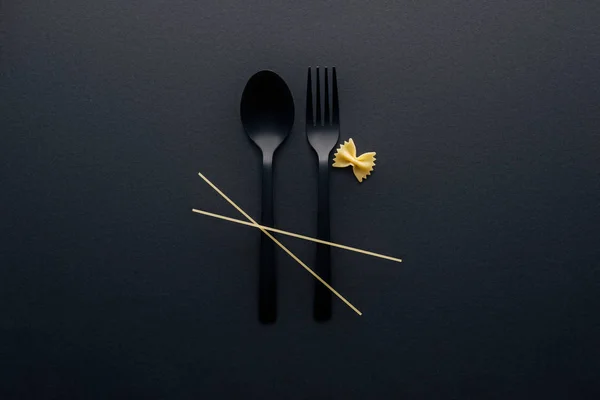 Vue du dessus des nouilles spaghetti sur des couverts en plastique près des pâtes farfalle sur fond noir — Photo de stock