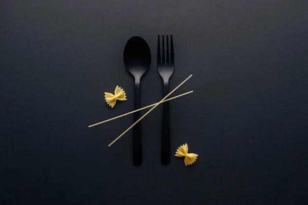 Plastic spoon and fork with farfalle pasta and spaghetti on black background — Stock Photo