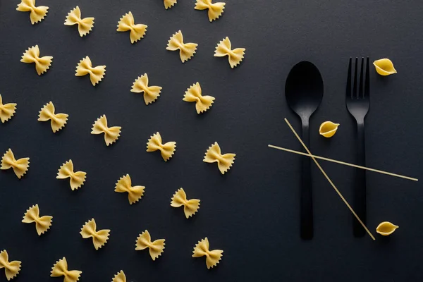 Colher de plástico e garfo com macarrão shell e espaguete perto farfalle massas no fundo preto — Fotografia de Stock