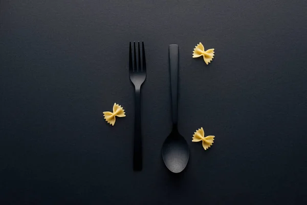 Vue du dessus de la cuillère à l'envers et fourchette près des pâtes farfalle sur fond noir — Photo de stock