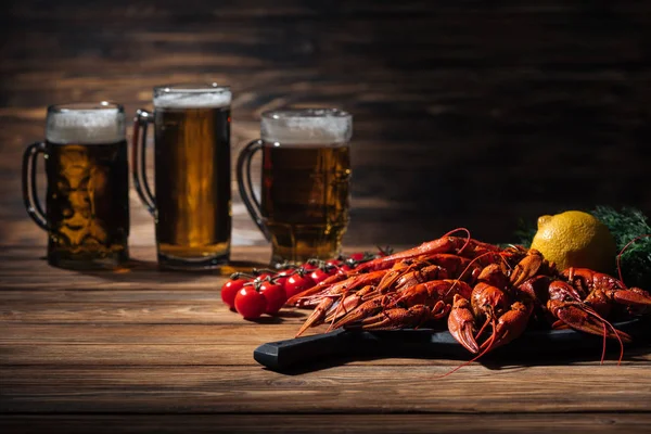 Foco seletivo de lagostas vermelhas, tomates, endro, limão e copos com cerveja na superfície de madeira — Fotografia de Stock