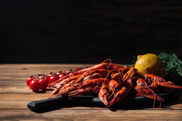 Red lobsters, tomatoes, dill and lemon on wooden surface — Stock Photo