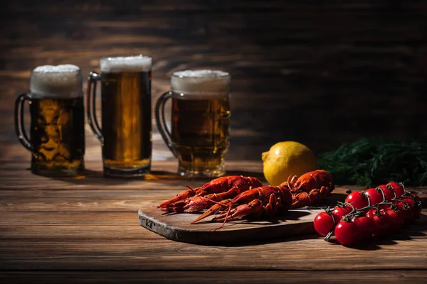 Селективный фокус красных омаров, помидоров, укропа, лимона и стаканов с пивом на деревянной поверхности — стоковое фото