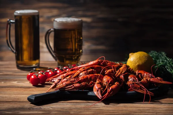 Red lobsters, tomatoes, dill, lemon and glasses with beer on wooden surface — Stock Photo