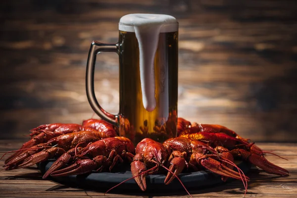 Vetro con birra e schiuma sul piatto con aragoste rosse sulla superficie di legno — Foto stock