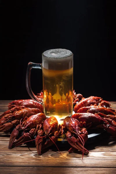 Verre avec bière et mousse sur plaque avec homards rouges à la surface en bois — Photo de stock