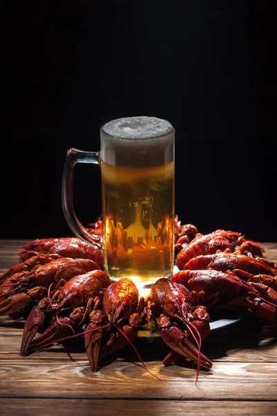 Vaso con cerveza y espuma en plato con langostas rojas en la superficie de madera - foto de stock