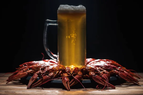 Glass of beer on plate with red lobsters at wooden surface — Stock Photo