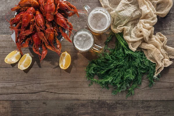 Draufsicht auf rote Hummer, Dill, Zitronenscheiben, Biergläser und Textiltuch auf Holzoberfläche — Stockfoto