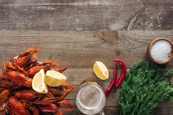 Vista dall'alto di aragoste rosse, aneto, fette di limone, pepe, bicchieri con birra e sale sulla superficie di legno — Foto stock