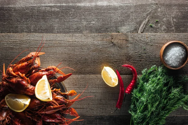 Vista superior de lagostas vermelhas, endro, fatias de limão, pimenta e sal na superfície de madeira — Stock Photo