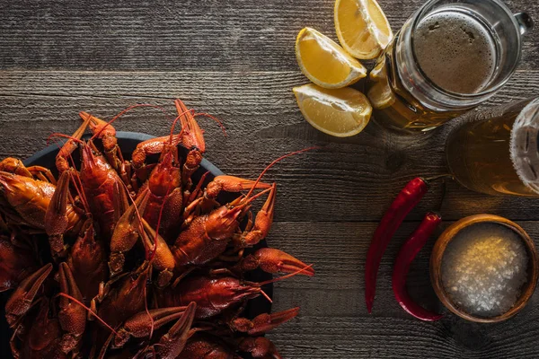 Vista superior de lagostas vermelhas, fatias de limão, pimentas, copos com cerveja e sal na superfície de madeira — Fotografia de Stock