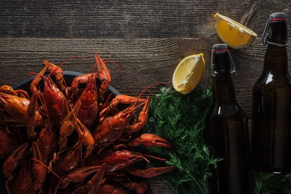 Vista superior de lagostas vermelhas, endro, fatias de limão, garrafas com cerveja na superfície de madeira — Fotografia de Stock