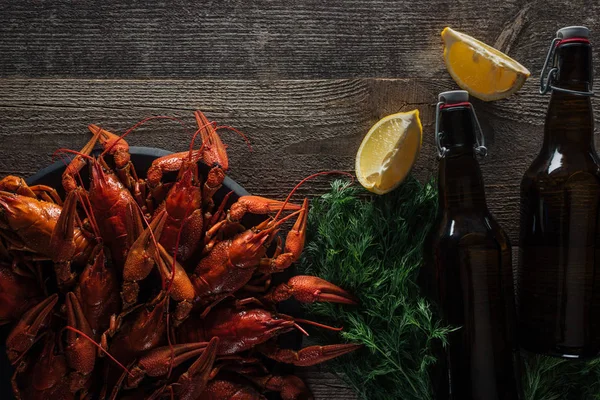 Vista superior de langostas rojas, eneldo, rodajas de limón, botellas con cerveza en la superficie de madera - foto de stock