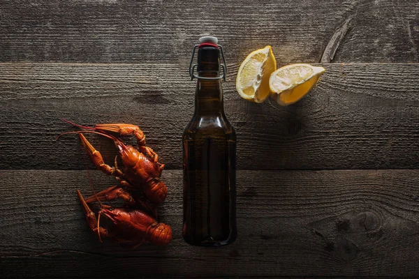 Vista superior de langostas rojas, rodajas de limón y botella con cerveza en la superficie de madera - foto de stock