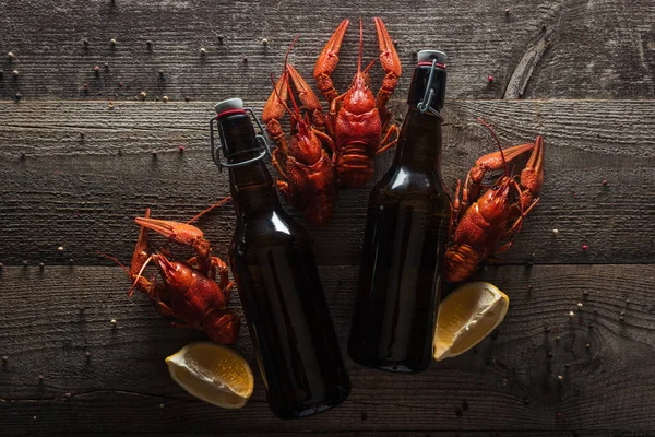 Вид сверху на красных омаров, ломтики лимона и бутылки с пивом на деревянной поверхности — стоковое фото