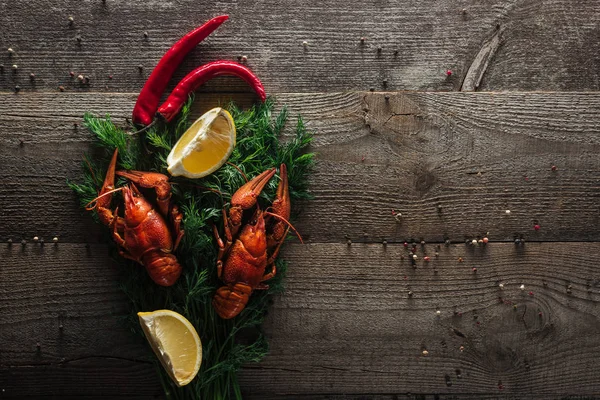 Top view of red lobsters, lemon slices, pepper and dill on wooden surface — Stock Photo