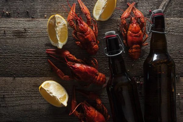 Vista superior de lagostas vermelhas, fatias de limão e garrafas com cerveja na superfície de madeira — Stock Photo