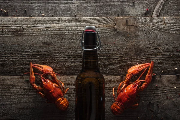 Top view of red lobsters and bottle with beer on wooden surface — Stock Photo