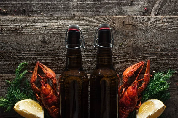 Vista superior de langostas rojas, eneldo, rodajas de limón y botellas de vidrio con cerveza en la superficie de madera - foto de stock