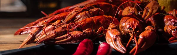 Panoramic shot of red lobsters with peppers on wooden surface — Stock Photo