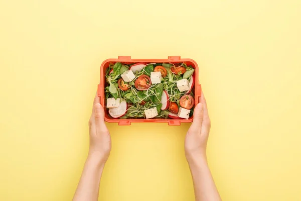 Vista recortada de la mujer sosteniendo lonchera con ensalada en las manos sobre fondo amarillo - foto de stock