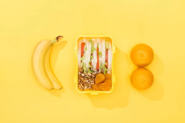 Top view of nuts, dried apricots with sandwiches in lunch box near bananas and oranges — Stock Photo