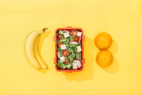 Top view of  lunch box with salad near bananas and oranges — Stock Photo