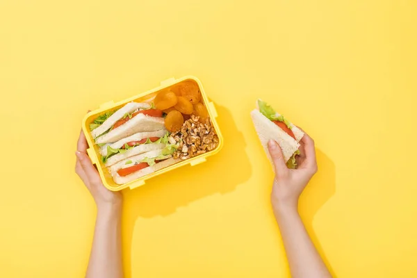 Cropped view of lunch box with nuts, dried apricots and sandwiches in woman hands — Stock Photo