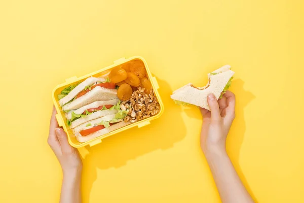 Vue recadrée de la boîte à lunch avec des noix, abricots secs et sandwichs dans les mains de la femme — Photo de stock