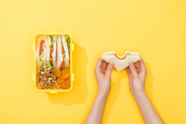 Cropped view of woman hold sandwich near lunch box with nuts, dried apricots and snacks — Stock Photo