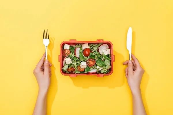 Vista recortada de la mujer sosteniendo tenedor y cuchillo sobre la lonchera con ensalada - foto de stock